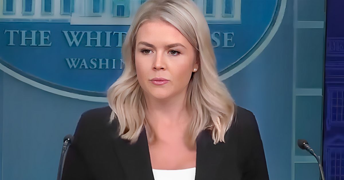 Karoline Leavitt at podium during press briefing, not wearing cross necklace